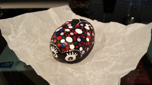 A painted ladybug rock sits on a piece of crinkled paper.