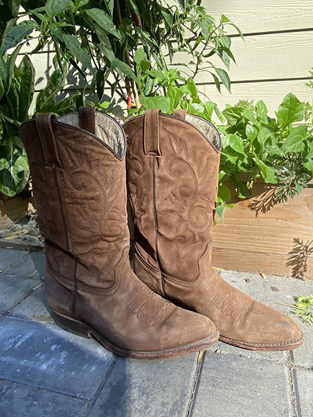Close-up of a pair of thrifted brown boots outside against some greenery.