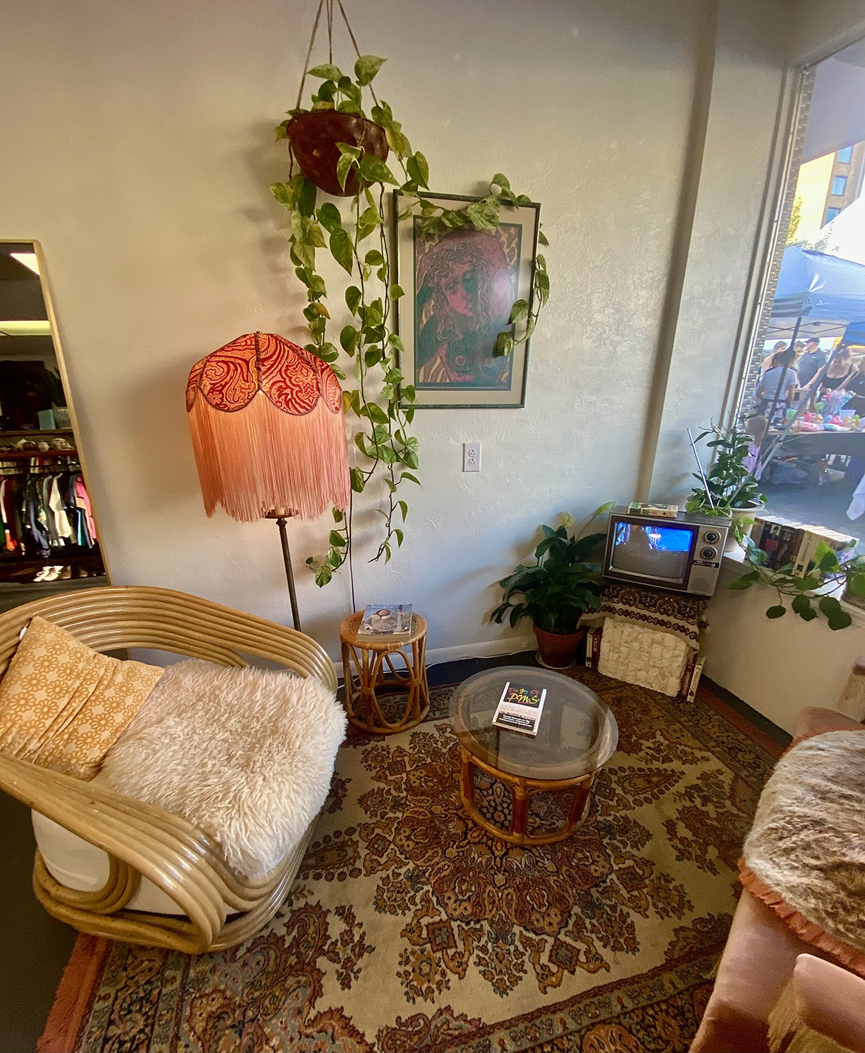 A cozy seating area inside a thrift shop. It has a tiny vintage television, a salmon-coloured floor lamp, and a plant hanging from the wall.