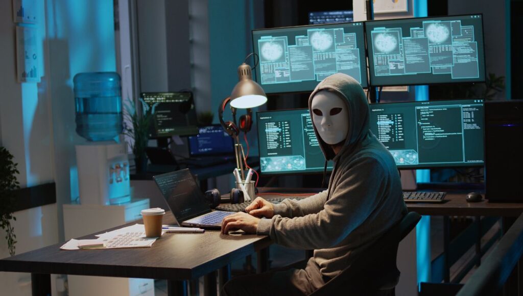 Masked man behind a desk in a computer lab.